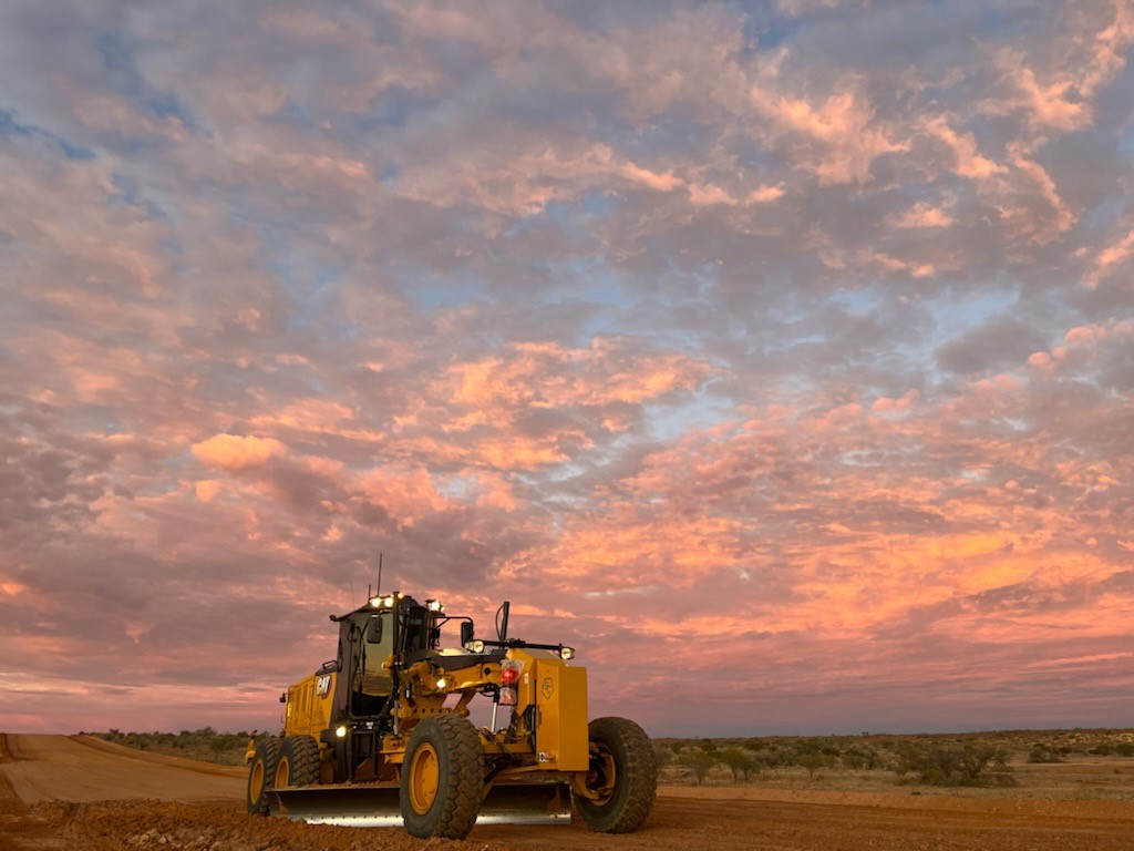 A grader layering the sand beside white board